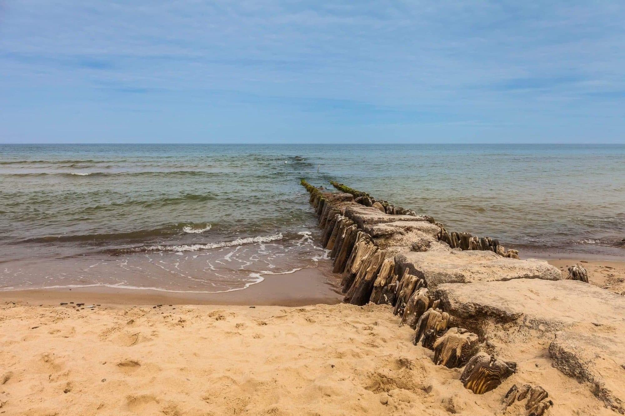 Kamienno-drewniany falochron na plaży w Sarbinowie w letni dzień
