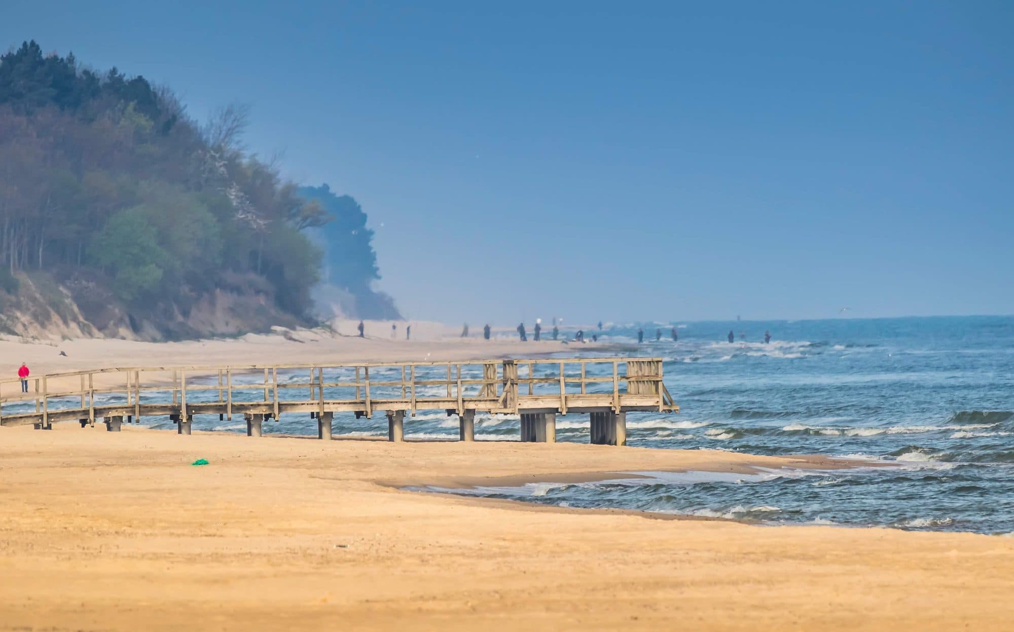 Molo i szeroka plaża w Sarbinowie z klifem i lasem w tle