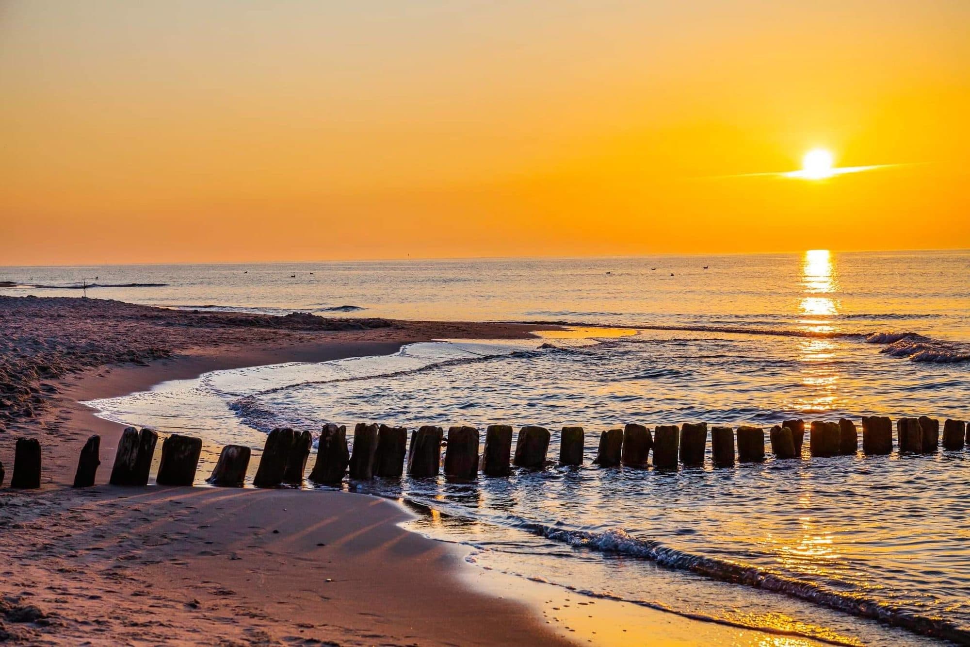 Złoty wschód słońca nad morzem w Sarbinowie — falochron i pusta plaża