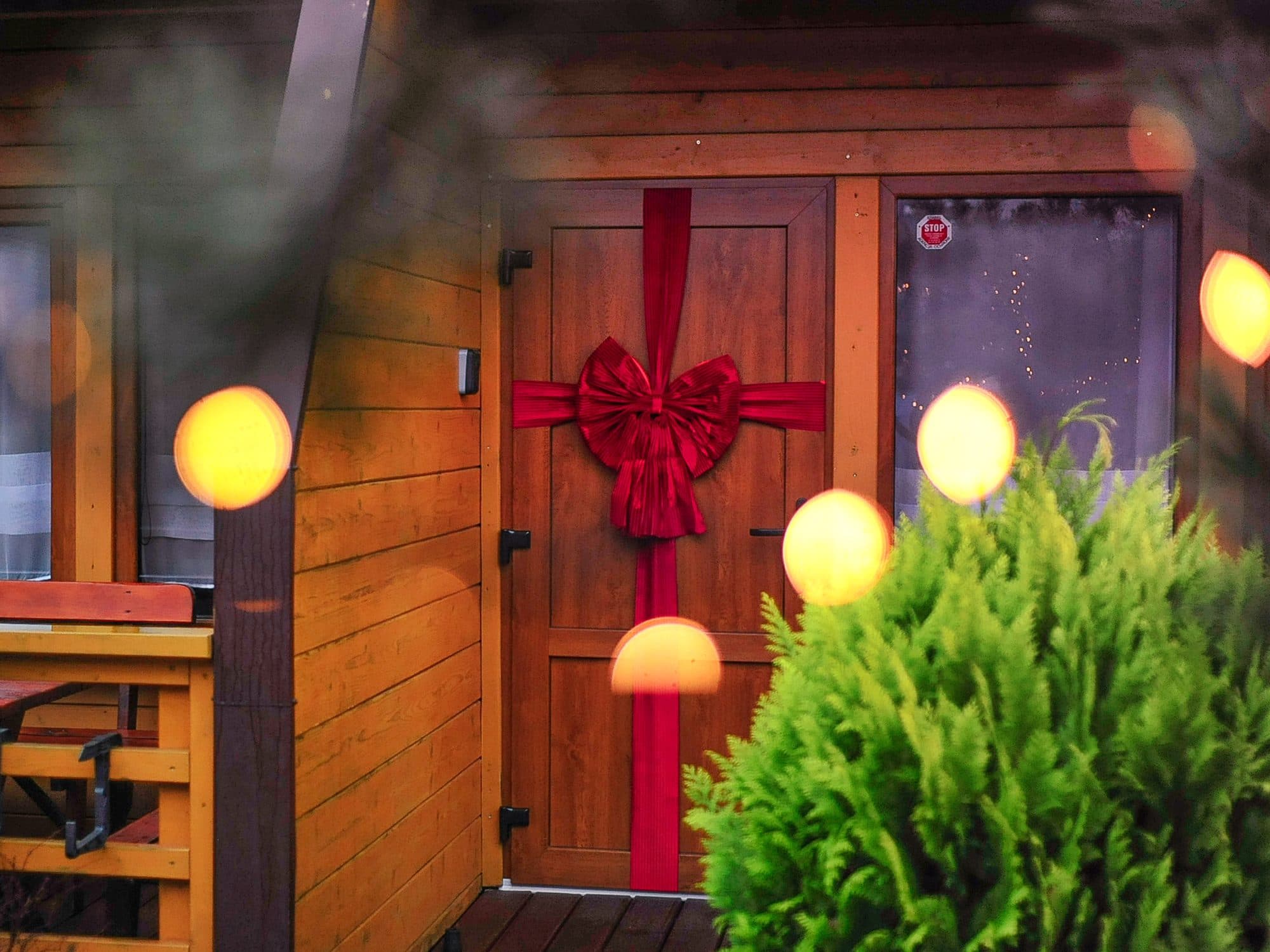 Red bow and fairy lights on the door of a wooden cottage in Sarbinowo